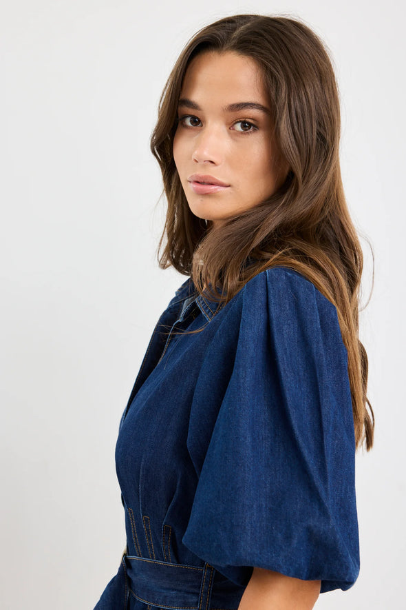 Dark indigo denim dress with a structured silhouette

Button-down front and panel seam detailing

D-ring belt for an adjustable, flattering fit

Soft puff sleeves with gentle volume

80% Cotton, 20% Polyester – durable yet comfortable

Style it casual or elevated for endless versatility