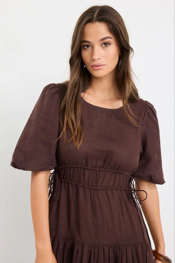 100% linen for breathable, natural comfort

Puff sleeves with soft volume for a feminine touch

Adjustable waist ties for a custom fit

Tiered skirt adds movement and flow

Midi length for timeless, versatile styling

Chocolate brown hue for an elegant, earthy look

Perfect for both casual wear and dressier occasions