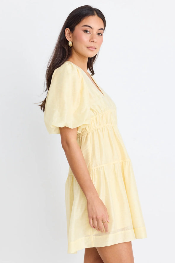 Get ready to indulge in the buttery softness of this yellow mini dress! Its playful tiered design and elastic waist provide both a comfortable fit and a feminine look. With a v neckline and drapey puff sleeves, this dress flatters your silhouette. And don't forget the charming bow and open back for added flair!