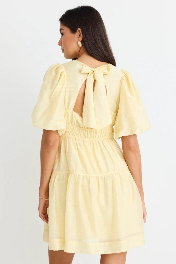 Get ready to indulge in the buttery softness of this yellow mini dress! Its playful tiered design and elastic waist provide both a comfortable fit and a feminine look. With a v neckline and drapey puff sleeves, this dress flatters your silhouette. And don't forget the charming bow and open back for added flair!