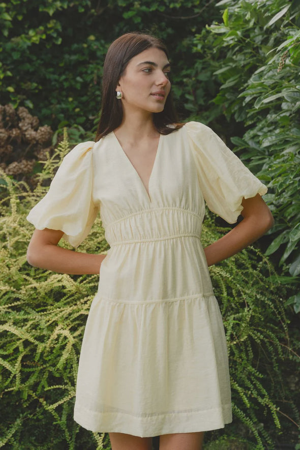 Get ready to indulge in the buttery softness of this yellow mini dress! Its playful tiered design and elastic waist provide both a comfortable fit and a feminine look. With a v neckline and drapey puff sleeves, this dress flatters your silhouette. And don't forget the charming bow and open back for added flair!