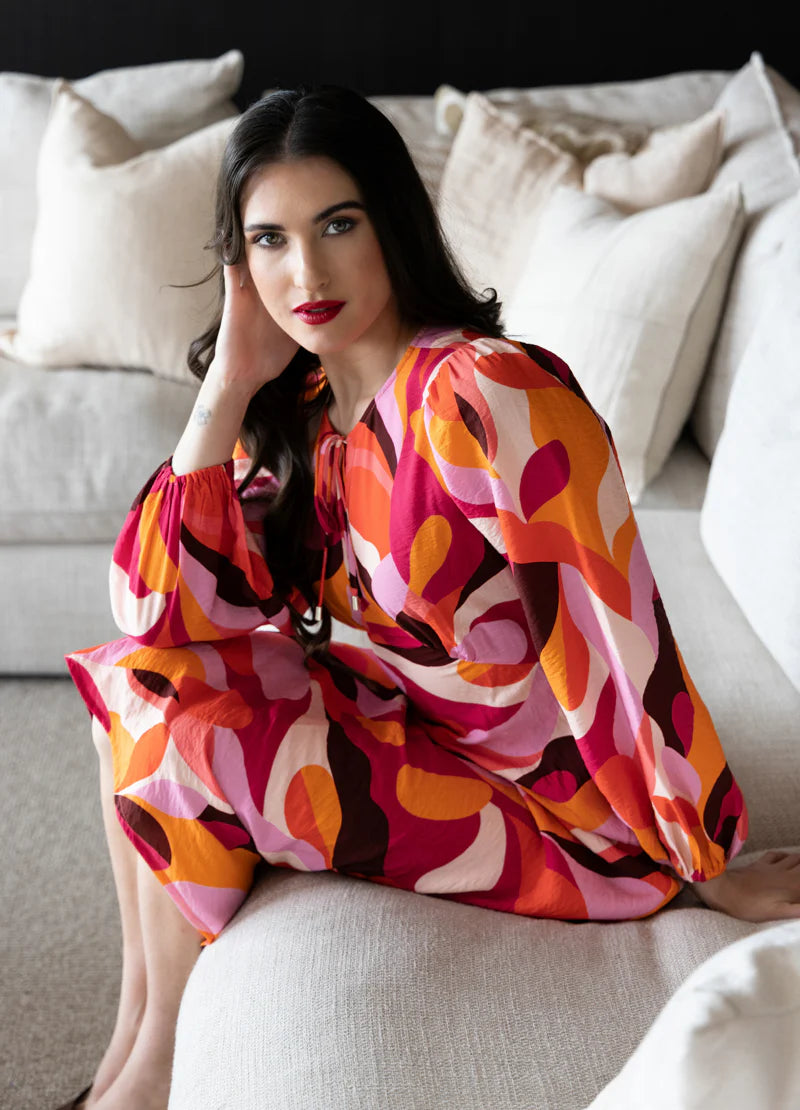 Elevate your wardrobe with our stunning long-sleeved maxi dress, crafted from a fun bright patterned fabric that effortlessly blends style and comfort. Featuring a flattering round neck with a v-neck detail and tie, this dress showcases a shaped empire bust for a feminine silhouette. The elastic cuff detail adds a touch of sophistication, while the convenient back neck zip ensures easy wear.