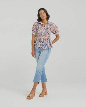 This short-sleeved shirt brings a playful touch with its softly puffed sleeves and delicate smocking that hugs the body. The gathered waist flares out into a subtle peplum, adding a flirty flair that flatters your silhouette. With refined tailoring and just the right amount of volume, it balances comfort and charm perfectly—ready to dress up your day or add fun to your casual look.