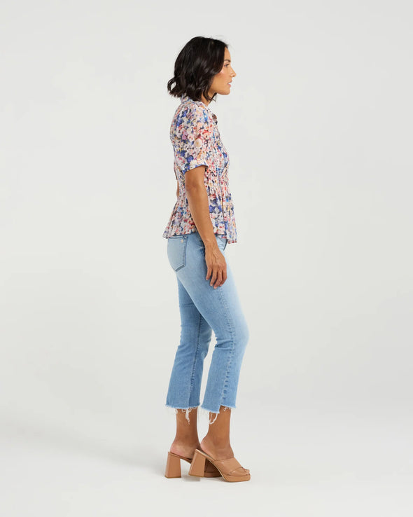 This short-sleeved shirt brings a playful touch with its softly puffed sleeves and delicate smocking that hugs the body. The gathered waist flares out into a subtle peplum, adding a flirty flair that flatters your silhouette. With refined tailoring and just the right amount of volume, it balances comfort and charm perfectly—ready to dress up your day or add fun to your casual look.