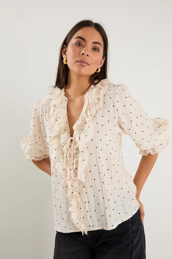 The Garnish top combines effortless charm with a playful touch. Featuring soft mid sleeves, a button front, and delicate ruffle trim, it offers subtle romantic details. The cream base adorned with black spots ensures a timeless yet lively look, while the lightweight fabric blend provides a graceful, flattering drape.