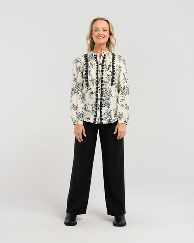 Say hello to Seduce's Abigail Blouse - a chic long-sleeve shirt, crafted with a relaxed fit and adorned with a timeless black floral pattern. The pleated upper bodice flatters your figure, while delicate lace along the placket adds a touch of feminine charm. Perfect for any occasion, this versatile piece combines style and refined details for a polished, modern look. Elevate your wardrobe with this exclusive design.