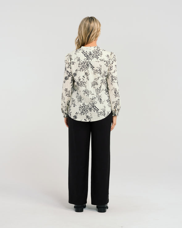 Say hello to Seduce's Abigail Blouse - a chic long-sleeve shirt, crafted with a relaxed fit and adorned with a timeless black floral pattern. The pleated upper bodice flatters your figure, while delicate lace along the placket adds a touch of feminine charm. Perfect for any occasion, this versatile piece combines style and refined details for a polished, modern look. Elevate your wardrobe with this exclusive design.